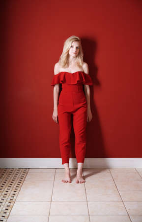 Beautiful young adult woman wearing red jumpsuit standing next to the wallの写真素材
