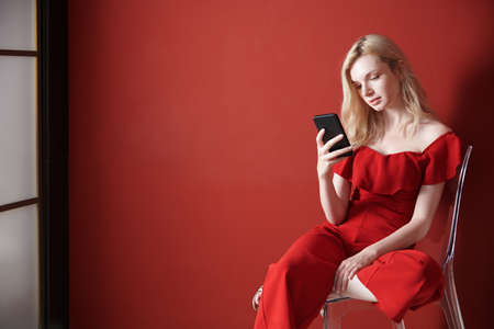 Young adult woman relaxing on a chair and using smartphoneの写真素材
