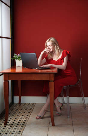 Young adult woman sitting at the table and working on laptopの写真素材