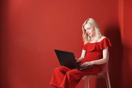 Young adult woman sitting on a chair and working on laptopの写真素材