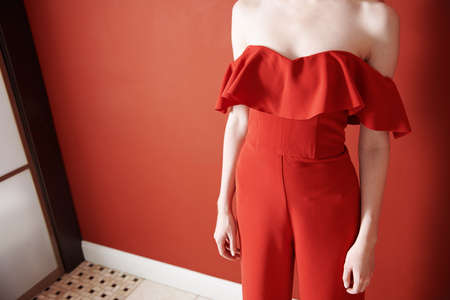 Young adult woman wearing red jumpsuit and standing next to the red wallの写真素材