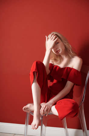 Beautiful young adult woman wearing red jumpsuit relaxing on chairの写真素材