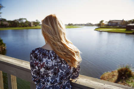 Retro styled woman standing on the wooden bridge and looking at the lakeの写真素材