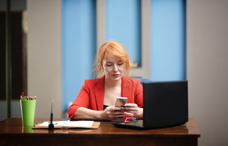 Redhead businesswoman using laptop and smartphone at the officeの写真素材