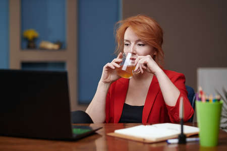 Businesswoman drinking tea while working on laptop at the officeの写真素材
