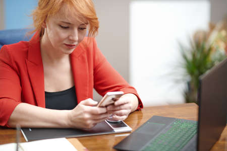 Redhead businesswoman using laptop and smartphone at the officeの写真素材