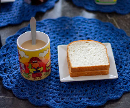 breakfast on a granite table with a white square plate and a colorful patterned cup of latte, slices...