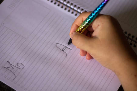 Handwritten letter A, female hand holding a colored pen in the shape of a mermaid tail, in a white spiral notebook, on a granite tableの写真素材