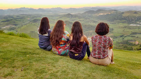 Group of friends sitting on the hill and looking at the sunset.の写真素材