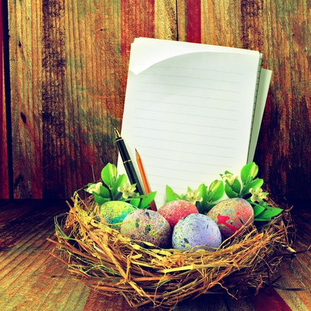 Easter eggs in hay nest. With flower, pen, pencil, papers and vintage backgroundの写真素材