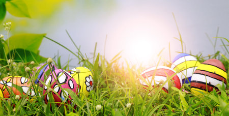 Colorful easter eggs on green grass with sun flare background.