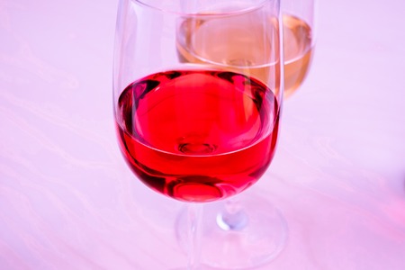 Two glasses with white and red wine on a light wooden background in pink lightの写真素材
