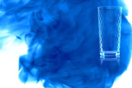 Empty glass of water on white background enveloped in puff of blue smoke.