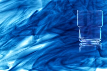 An empty glass for whiskey on white background enveloped in puff of blue smoke.