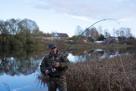 A man catches fish in the lake. Around the autumn - dry grass, trees with fallen leaves. The lake...