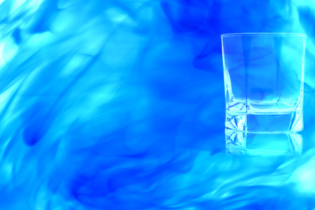 An empty glass of whiskey on white background enveloped in puff of blue smoke.の写真素材