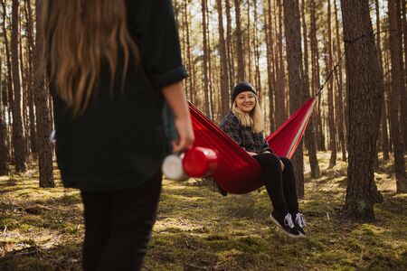 Happy young hipster girl enjoys life and nature on hammock with other woman in the summer forest.の写真素材
