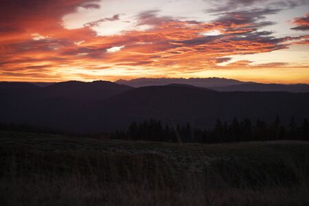 Autumn sunrise over Tatra Mountains national park in Poland. Panoramic breathtaking photo. Tatras in the background. Hills and trees in the foreground. Burning sky with clouds over the mountains.の写真素材