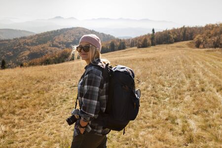 smiling woman in a cap and sunglasses with backpack hiking the mountains. A beautiful morning in the...