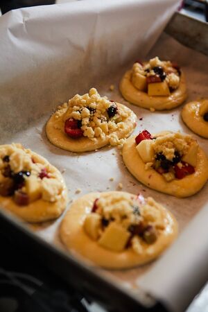 homemade buns with fruit and crumble on white baking paper ready for baking in the oven.の写真素材