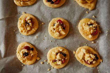 homemade buns with fruit and crumble on white baking paper ready for baking in the oven. selective focus, top viewの写真素材