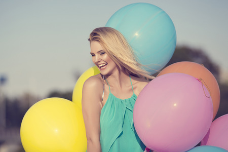 beautiful blonde happy woman with colorful pastel balloons in the cityの写真素材