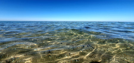 Gentle waves and currents near the coast, water surface and sea horizon under the clear blue sunny summer sky in Brighton Beach, Adelaide, Australiaの写真素材