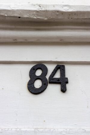 Old black house number 84 on a white wooden doorの写真素材