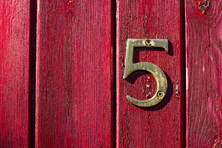 Bronze house number five on a weathered red front door