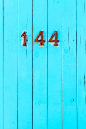 House number 144 on a bright turquoise wooden front door