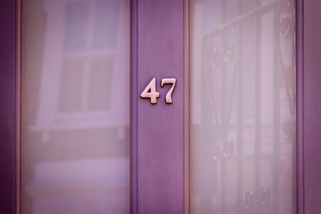 House number 47 on a pale purple wooden front door with large glass windows reflecting a house...