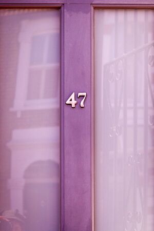 House number 47 on a pale purple wooden front door with large glass windows reflecting a house oppositeの写真素材