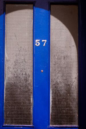 House number 57 on a royal blue wooden front door with dirty window panes in Londonの写真素材