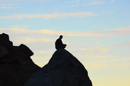 Meditating man sitting on top of a rock in the mountains の写真素材