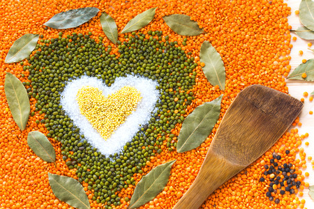 Heart shape made of mixed wheat grains, salt, green mung beans, orange red lentils and bay leaves on table surface with wooden spatula and black pepper, top view. Dry cooking ingredients for a healthy soup.
の写真素材