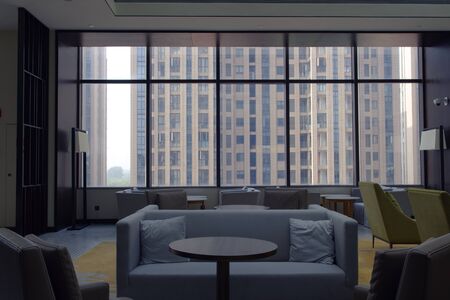 Blue couches in stylish room, high ceiling. Minimal lounge in front of glass window and high rise building view.の写真素材