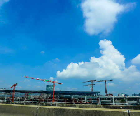 cranes in construction area looking from the highway on blue sky with clouds backgroundの写真素材