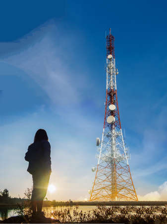 Black silhouette of young women seeing at  telecommunication tower on blue sky background