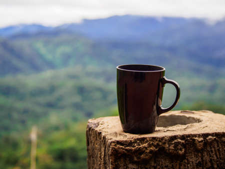black cup of coffee on the cement pillar on blur mountain and forests background in the morning