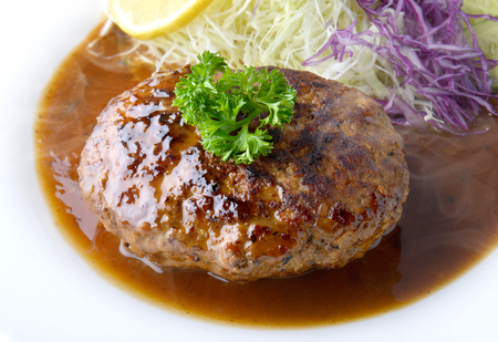 Japanese style hamberger or hamberg serve with gravy sauce and vegetables salad in low studio lighting.の写真素材