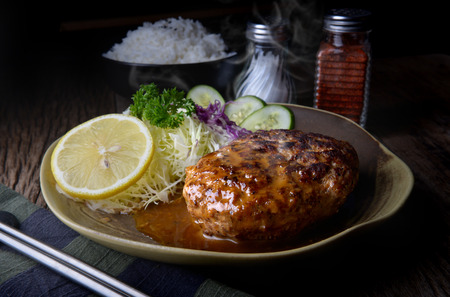 Japanese style hamberger or hamberg serve with gravy sauce and vegetables salad in low studio lighting.の写真素材