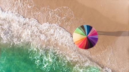 Colorful of umbrella on the beach and foam of sea wave from top eye view photo in outdoor sunlight lighting.の写真素材