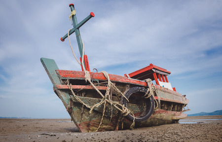 Wreck wooden fishery boat on the beach with blue and cloud sky.の写真素材