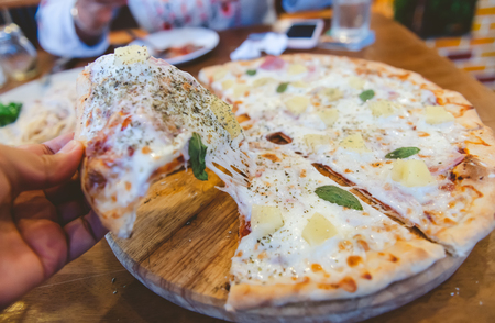 Stretch cheese piece of homemade pizza cutting party with indoor lighting.の写真素材