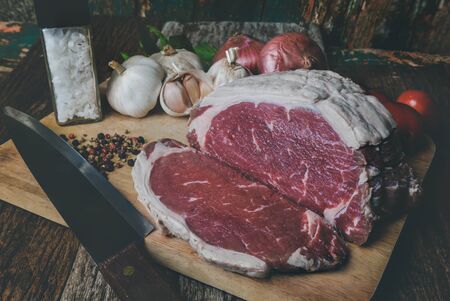 Raw beef cutting for steak with seasoning ingredient on wooden plate with grey and dark low lighting.の写真素材
