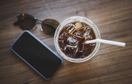 Ice americano coffee in plastic glass on wooden table with indoor warm lighting in relaxing concept.の写真素材