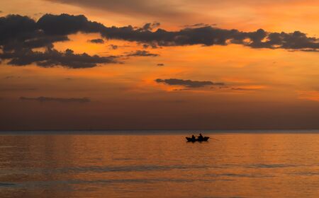 Silhouette of boat and fisherman with warm and sunset low lighting dark shadow view.