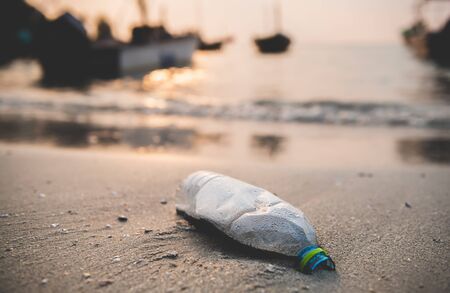 Plastic bottle on the beach with outdoor sun set low lighting and dark shadow.