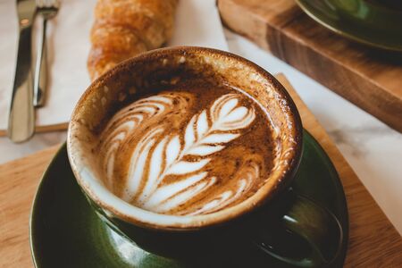 Hot coffee cappuccino latte art serve with croissant in morning worm lighting.の写真素材