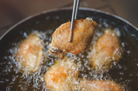 Frying salt chicken wing with cooking oil in iron pan with indoor low lighting.の写真素材